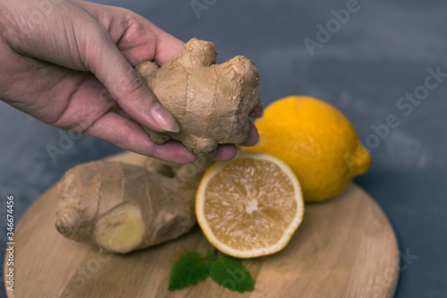fresh ginger root with a lemon in a woman hands and mint or mellis leaves on a gray background and a wooden board. Cold and virus protection photo