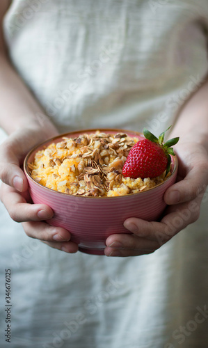 Pink plate of corn porridge with granola and strawberry in the hands of a girl. Healthy, diet, vegan or food concept for social media.