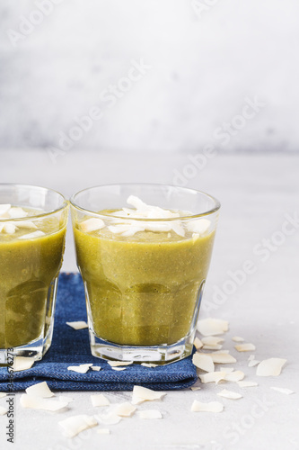 Green smoothies with coconut flakes in glass on denim napkin, gray background. Health content, healthy diet. Vertical format