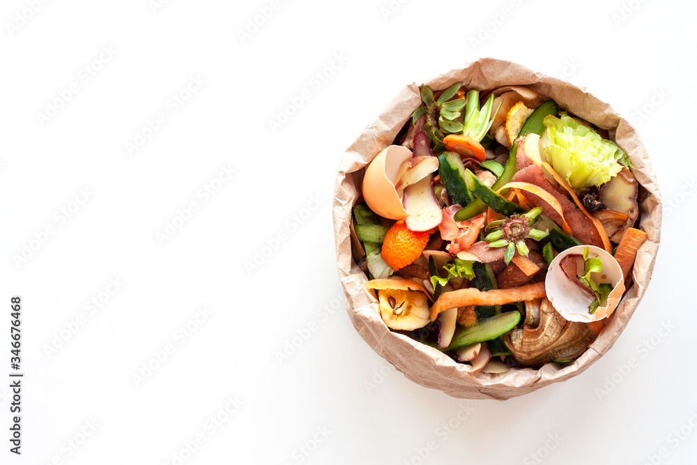Organic food waste in paper bag on white kitchen table. Vegetable peelings and food leftovers ready to compost. Environmentally responsible behavior, ecological, recycling waste concept. Copy space.