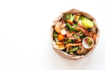 Organic food waste in paper bag on white kitchen table. Vegetable peelings and food leftovers ready to compost. Environmentally responsible behavior, ecological, recycling waste concept. Copy space.