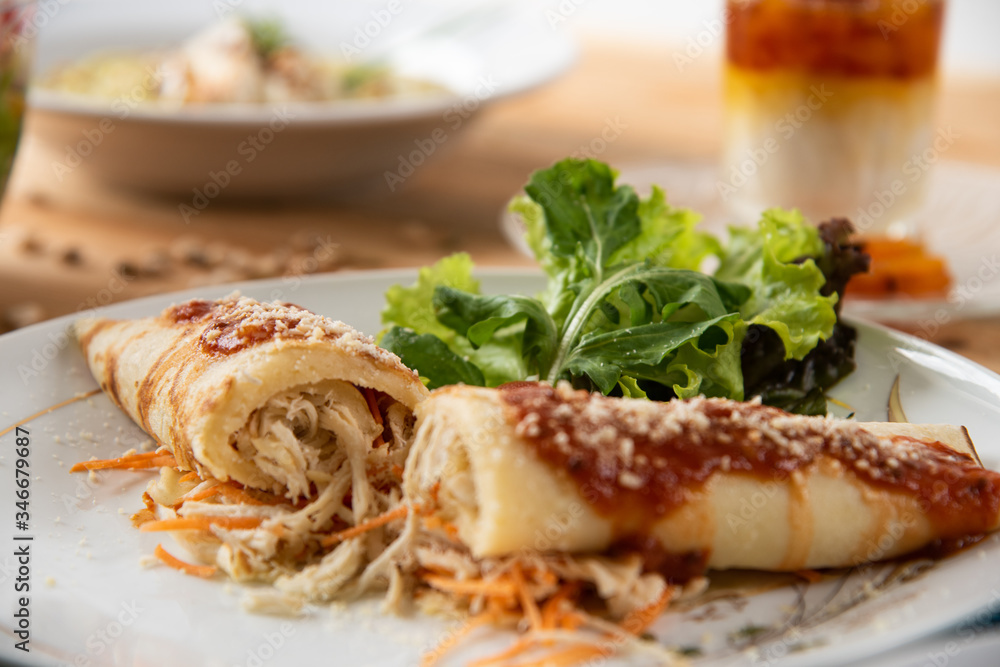 Chicken pancake on top of a white plate on a wooden table with salads in the background. Brazilian pancake