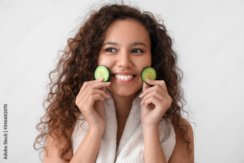 Beautiful young African-American woman with cucumber slices on light background Beautiful young African-American woman with cucumber slices on light background