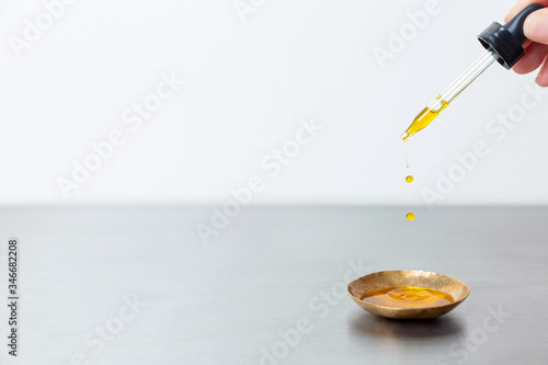 Oil serum tincture droplets squeezed from dropper into brass gold bowl on stainless surface photo