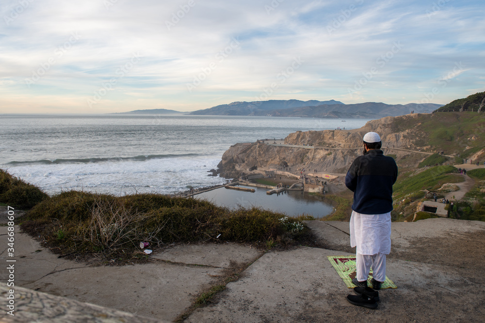 Man is praying on cliff at sunset ocean, San Francisco, California
