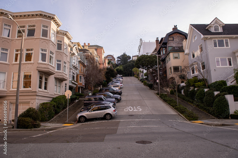 A steep residential street with rows of houses stepping up the hill and cars parked on the street