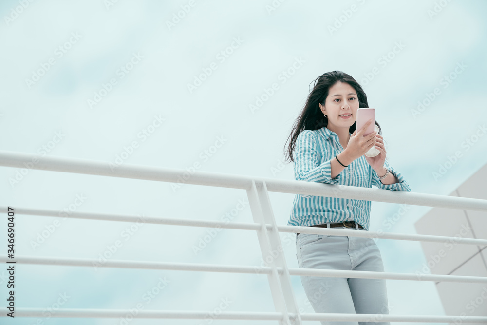 happy smiling young office lady having coffee break time and stay alone on rooftop of office building skyscraper. joyful business woman worker texting chatting online with friend leaning on railing happy smiling young office lady having coffee break time and stay alone on rooftop of office building skyscraper. joyful business woman worker texting chatting online with friend leaning on railing