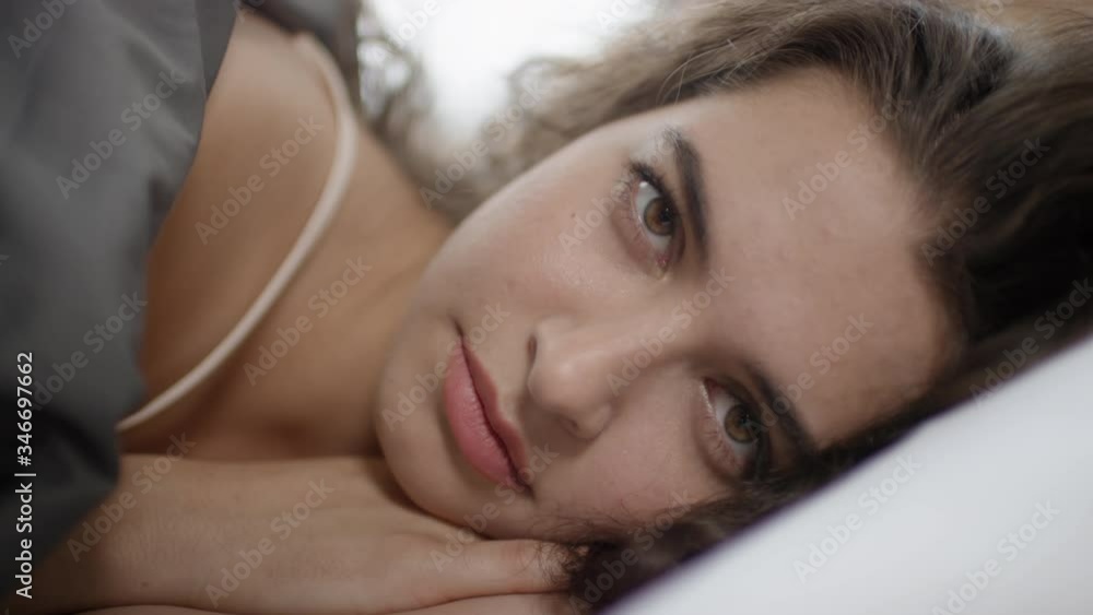Close up shot of beautiful young woman with brunette hair and brown eyes waking up in bed and looking at camera Close up shot of beautiful young woman with brunette hair and brown eyes waking up in bed and looking at camera