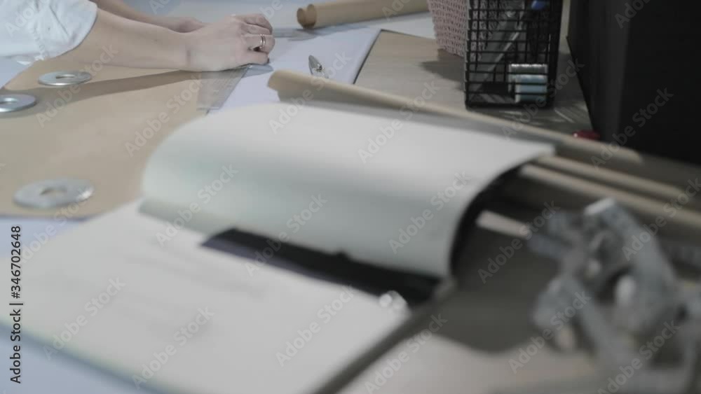Slow motion video of the fashion designer that works at the table with curves and a pattern, draws a soap slice, around lies scissors, centimeter, a notebook with sketch, sew studio, view from a top Slow motion video of the fashion designer that works at the table with curves and a pattern, draws a soap slice, around lies scissors, centimeter, a notebook with sketch, sew studio, view from a top