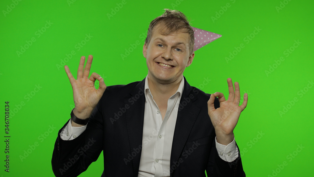 Drunk sleepy young businessman with hangover in festive cap showing OK sign Drunk sleepy young businessman with hangover in festive cap showing OK sign