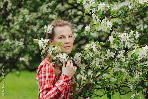 Beautiful young happy woman in a flowered garden. Girl among the flowers of apple trees, cherries. Springtime scene. Positive model in a casual style. Lifestyle
