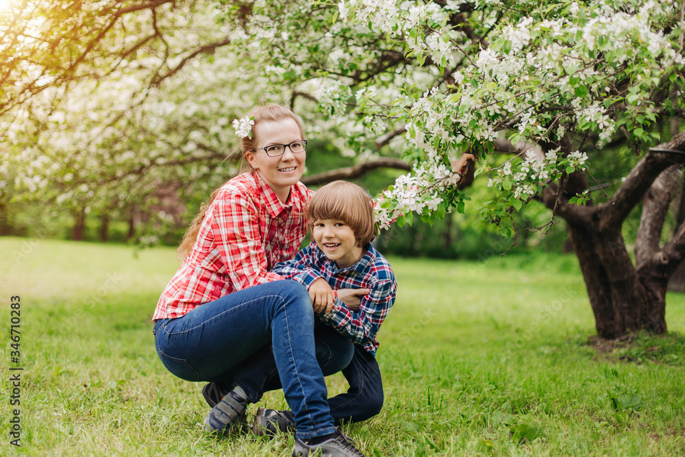 Fototapeta premium Mother and baby in blooming garden. Mom and child in spring. Springtime family scene. Flowers of apple or cherry tree.