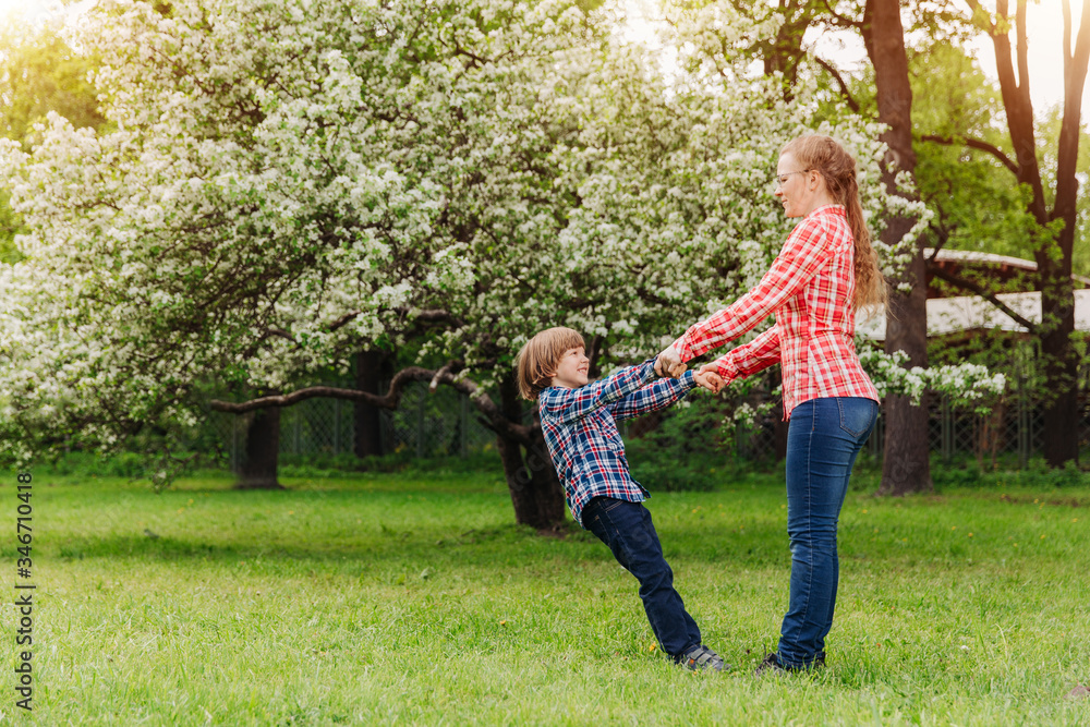 Fototapeta premium Mother and baby in blooming garden. Mom and child in spring. Springtime family scene. Flowers of apple or cherry tree.