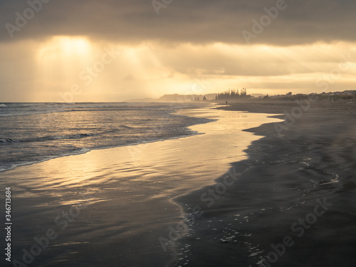 sun rays poking through clouds over ocean beach © Anita Burgess