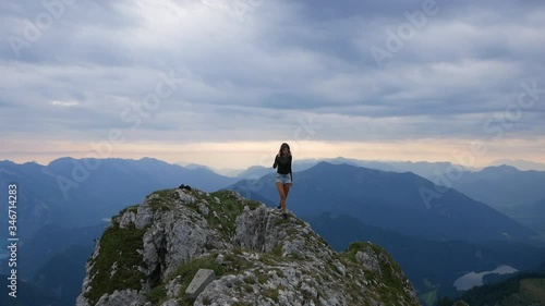 Young pretty hiker girl walking at mountain peak Schafberg Austria. 60fps slowmo footage. Sexy woman climbing in alpine scenery. Sunrise at summit and clouds dramatic epic mood photo