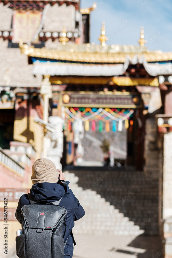 Young man traveler with sweater and backpack traveling in Songzanlin Temple, happy Photographer taking photo in trip Zhongdian city ( Shangri-La) Yunnan, China. Asia and Solo travel concept