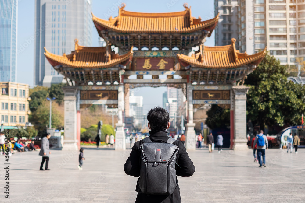 Young man traveler traveling at Jinbi square, golden Horse and Jade Rooster Archways. landmark and popular for tourists attractions in Kunming, Yunnan, China. Asia and Solo travel concept