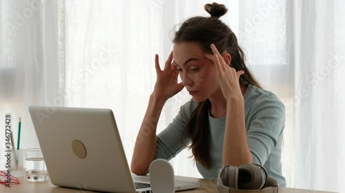 Tired self employed female in casual clothes sitting at table with netbook while working online and having problems with project