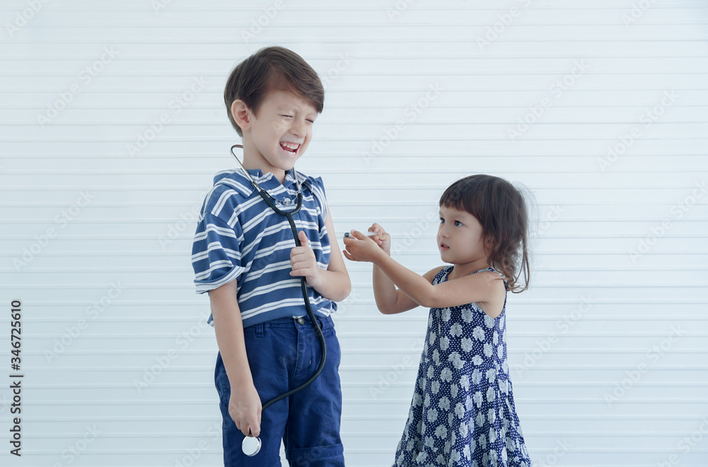 A caucasian little boy and girl playing together acted as doctor nurse patient at home. A cute younger sister use a syringe to pretend to inject her brother's arm A caucasian little boy and girl playing together acted as doctor nurse patient at home. A cute younger sister use a syringe to pretend to inject her brother's arm