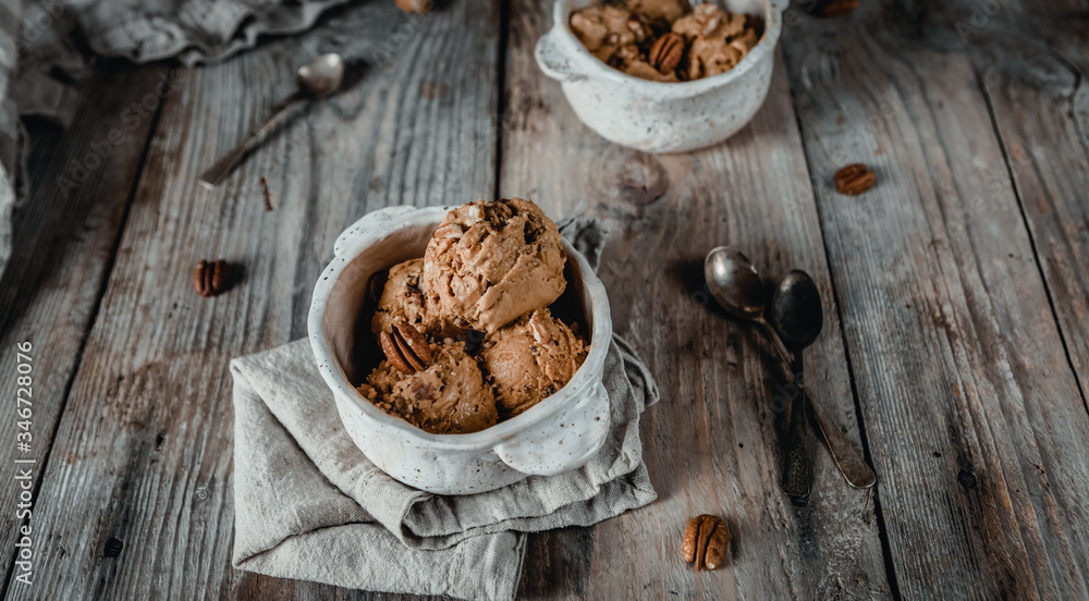 Fototapeta premium creamy caramel ice cream scoops with pecan nuts in white ceramic bowls on wooden table