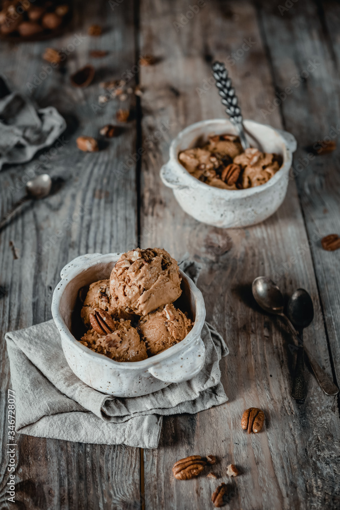 Fototapeta premium creamy caramel ice cream scoops with pecan nuts in white ceramic bowls on wooden table
