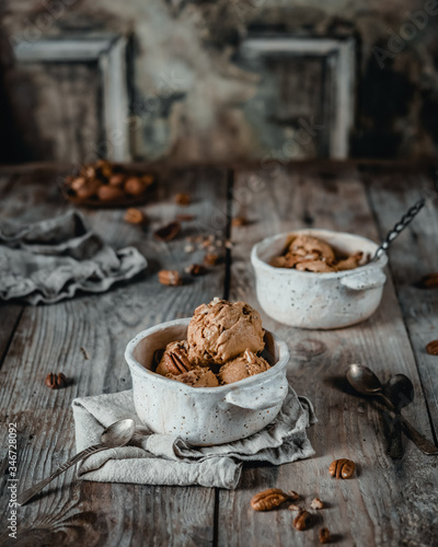 creamy caramel ice cream scoops with pecan nuts in white ceramic bowls on wooden table