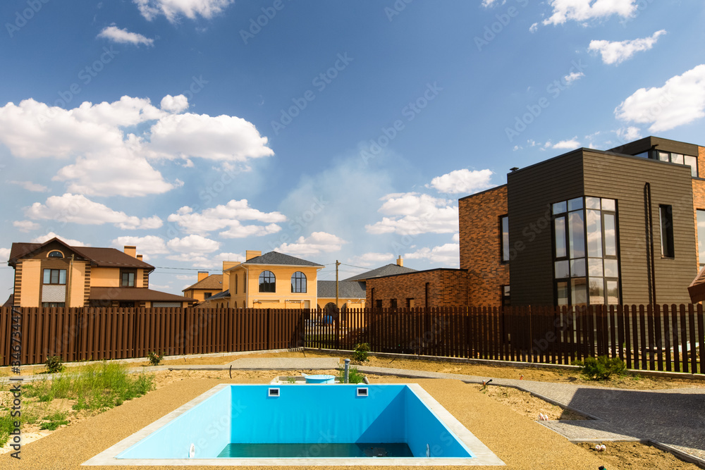 Back yard pool under construction. Empty Swimming Pool in the future garden. Modern cottages, blue sky white clouds.Residential compound.