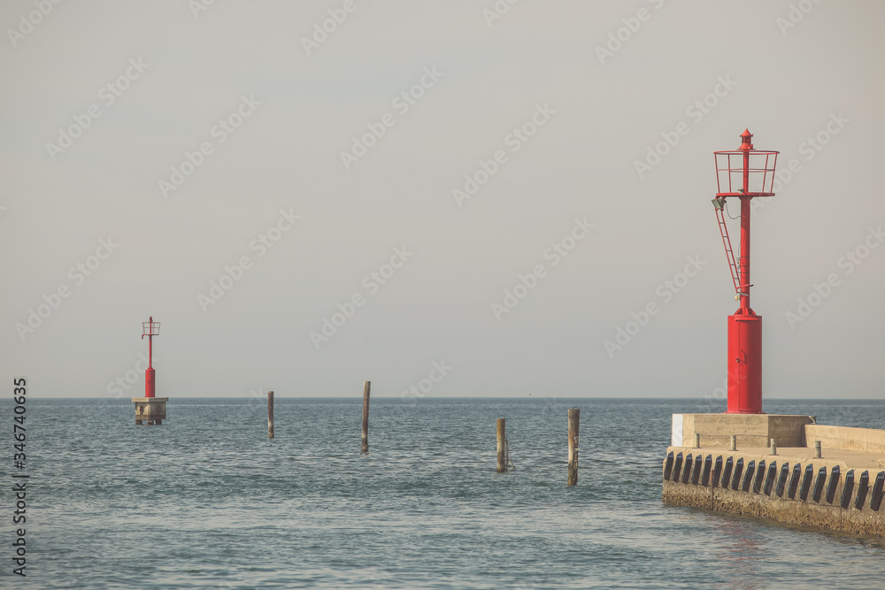 Two red safety light beacons on the sea. Small lighthouses on the entrance of a marina, leading ships to a safe landing.