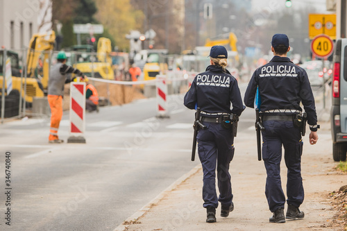 Male and female police officers walking on a pedestrian walkway past the construction zone on a road. Police inspecting work of road maintenance people or workers.