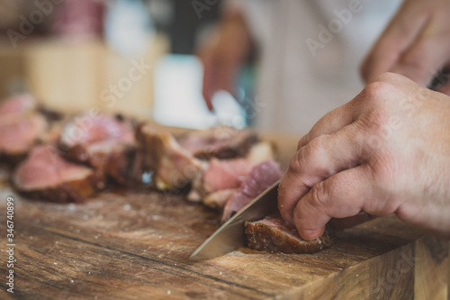Cutting or slicing beef meat into think chunks or steaks ready to eat. Visible hand with a sharp knife cutting the pieces of meat on an event.