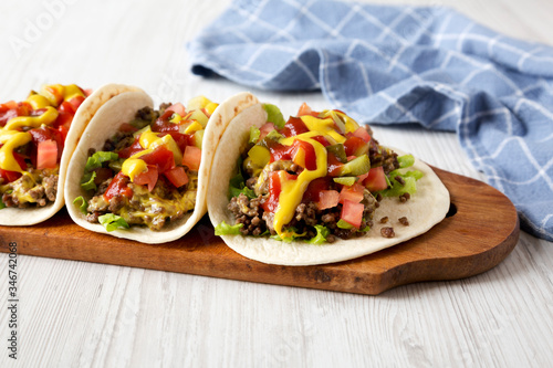 Homemade Cheeseburger Tacos on a rustic wooden board on a white wooden background, side view.