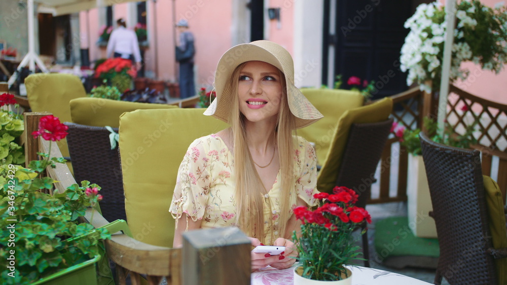 Smiling woman in outside restaurant. Cheerful young woman sitting at table in outside restaurant on cozy street.
