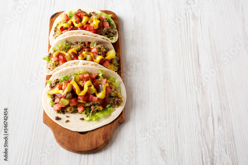 Homemade Cheeseburger Tacos on a rustic wooden board on a white wooden background, low angle view. Space for text.