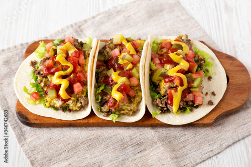 Homemade Cheeseburger Tacos on a rustic wooden board on a white wooden background, side view. Close-up.