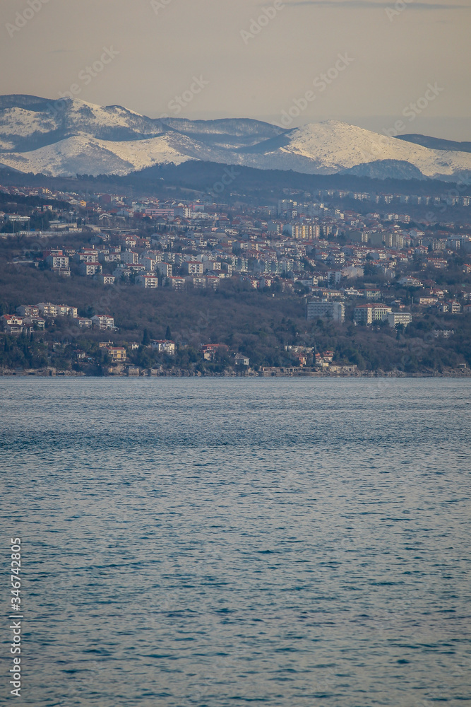 Panorama of the suburbs of Rijeka, Croatia in a cold winter day, with visible snow on the mountains in the background.