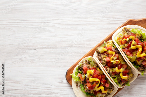 Homemade Cheeseburger Tacos on a rustic wooden board on a white wooden background, top view. Flat lay, overhead, from above. Copy space.