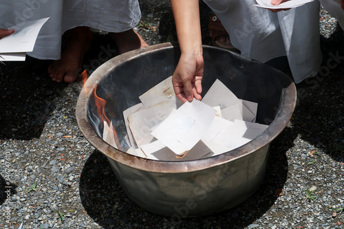 Woman hand putting  silver & gold paper on burning fire frame to make merit for dead person in funeral ceremony at Buddhist temple with traditional white cloths        