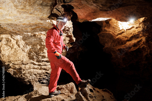 Man walking and exploring dark cave with light headlamp underground. Mysterious deep dark, explorer discovering mystery moody tunnel looking on rock wall inside. photo