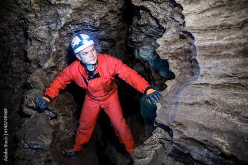 Man walking and exploring dark cave with light headlamp underground. Mysterious deep dark, explorer discovering mystery moody tunnel looking on rock wall inside. photo