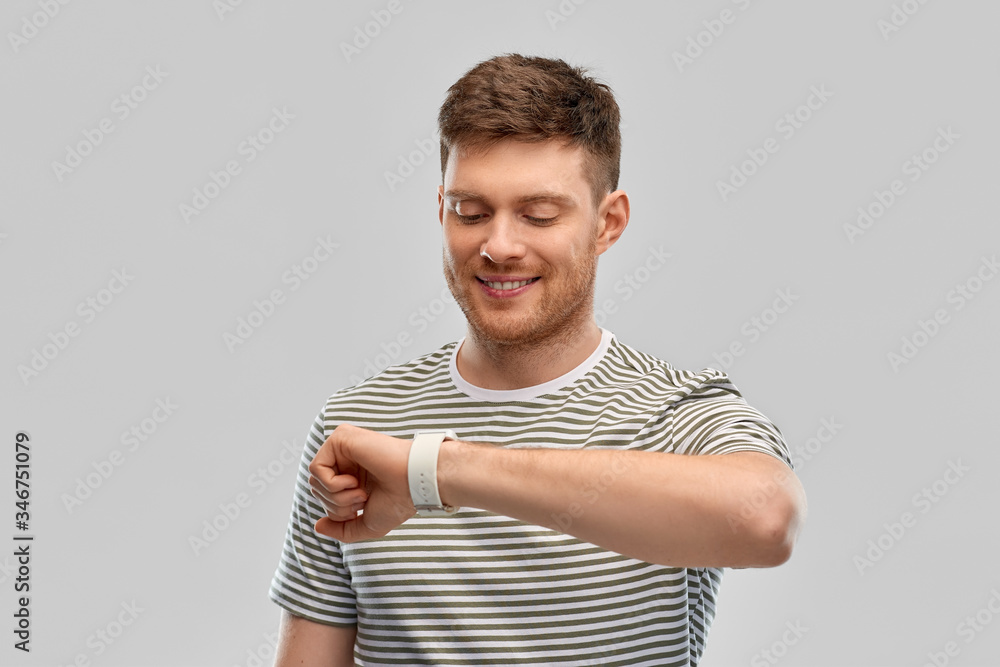 technology and people concept - smiling young man looking at smart watch over grey background technology and people concept - smiling young man looking at smart watch over grey background