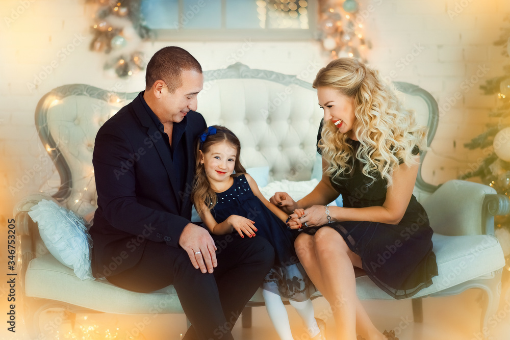 Family Christmas concept. Lovely family in dark fashionable clothes seat on sofa near decorated Xmas tree on winter evening. Happy household with daughter at home. Happy New year. Merry Christmas