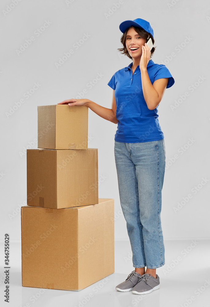 mail service and shipment concept - happy smiling delivery woman with parcel boxes calling on smartphone over grey background mail service and shipment concept - happy smiling delivery woman with parcel boxes calling on smartphone over grey background