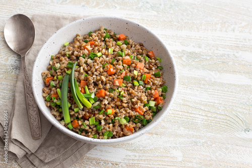 Delicious vegan buckwheat with vegetables and green onions on a light wooden background. Healthy homemade food