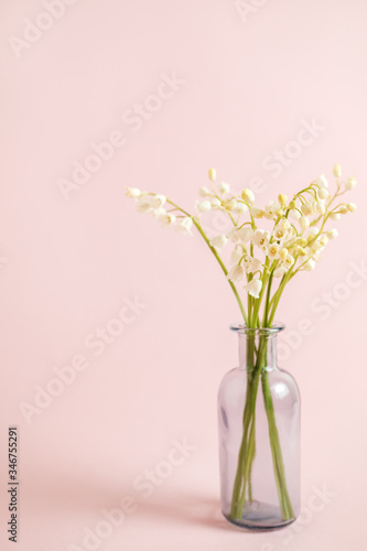 Greeting card with white lily of the valley on pink background for celebration Mothers Day, wedding, March 8. Nature concept. Home garden in vase. Summer green floral design. Selective focus.