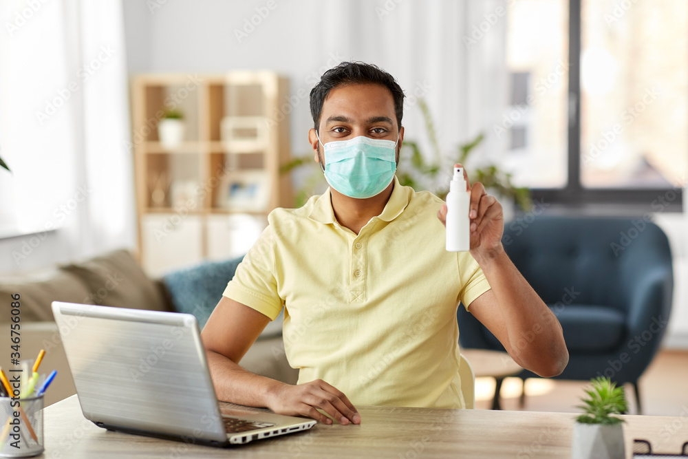 quarantine, remote job and pandemic concept - happy indian man wearing face protective medical mask for protection from virus disease with hand sanitizer and laptop computer working at home office quarantine, remote job and pandemic concept - happy indian man wearing face protective medical mask for protection from virus disease with hand sanitizer and laptop computer working at home office