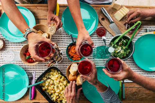 Above view of group of friends people eat and drink together celebrating and having fun toasting with red wine - coloured table and decoration - social contact and normal life scene with family