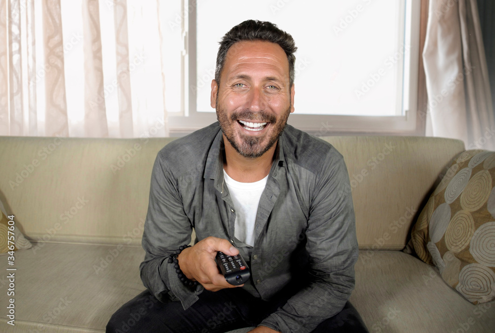 young attractive happy and relaxed man watching television show or comedy movie sitting at living room sofa couch enjoying in domestic entertainment young attractive happy and relaxed man watching television show or comedy movie sitting at living room sofa couch enjoying in domestic entertainment
