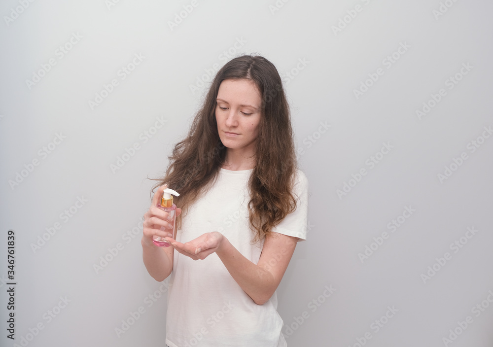 Young girl holding hand antiseptic, disinfectant on a grey background.