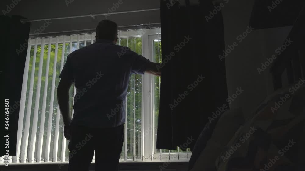 Man opens blinds in the morning on a bright beautiful day Man opens blinds in the morning on a bright beautiful day
