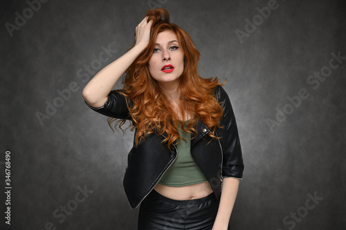 The girl demonstrates vivid emotions by changing poses. Portrait of a young pretty woman with beautiful hair and excellent make-up in a green T-shirt and a black jacket on a gray background.